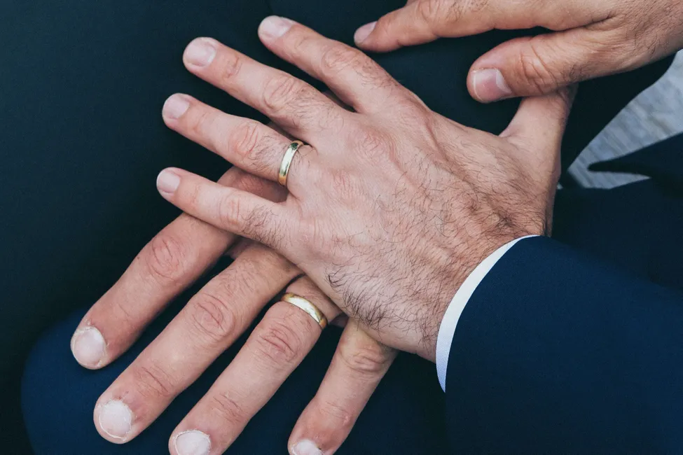 Close-up of two men holding hands with wedding rings